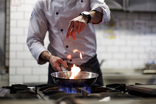 Chef seasoning a pan over a propane gas stove