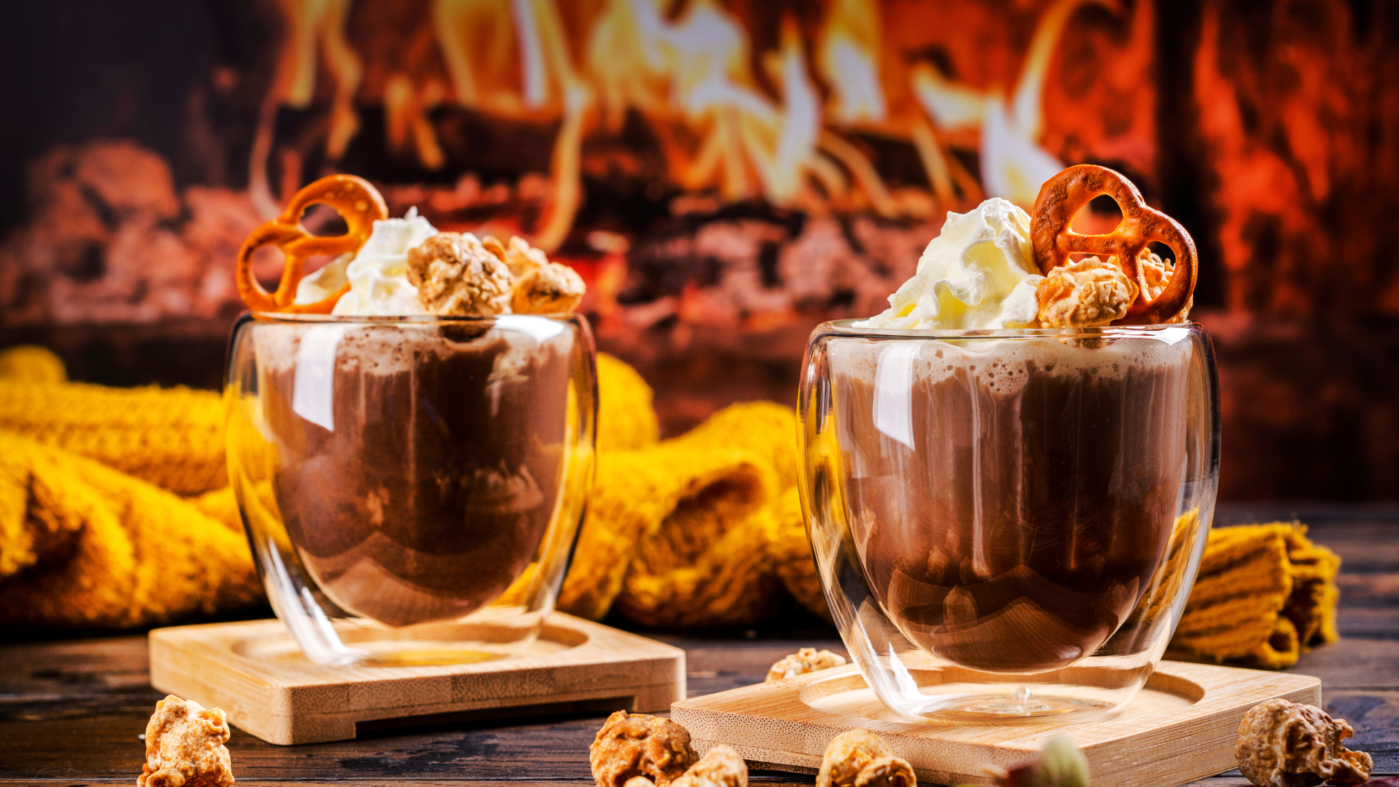 cozy winter recipes - two fancy glass cups with hot chocolate and whipped cream in front of a blazing indoor fireplace