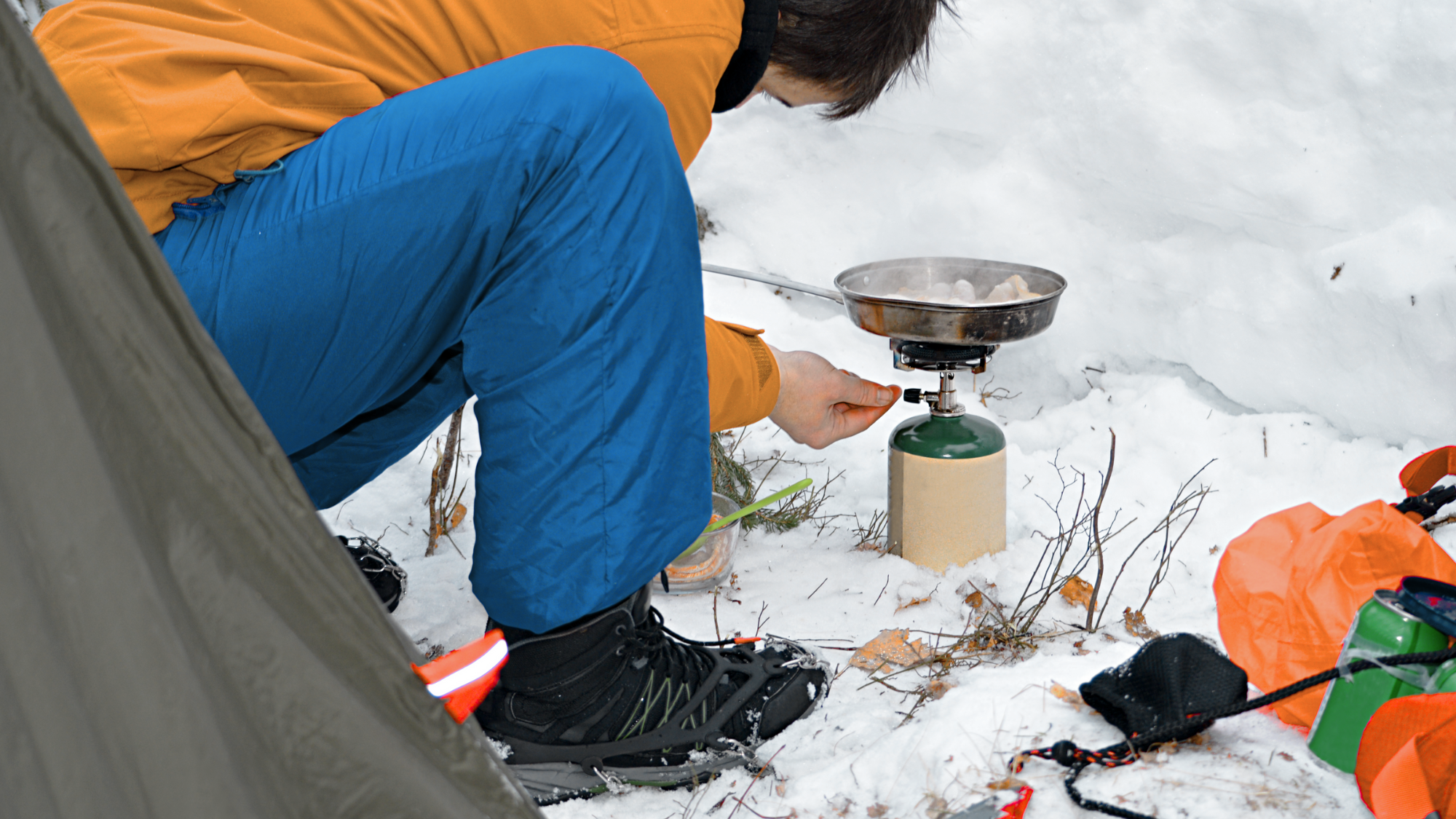 person lighting propane burner to cook while camping in snow