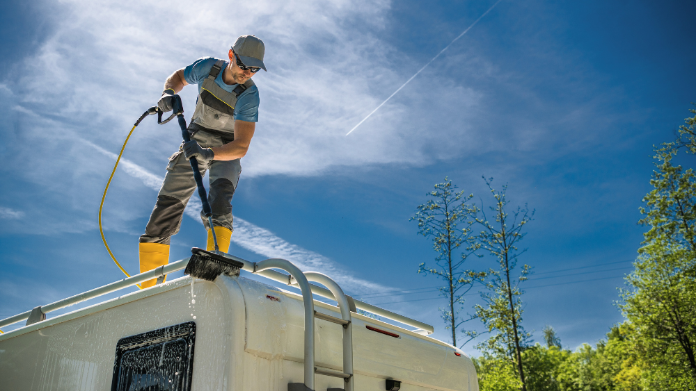 man de-winterizing rv camper for spring by cleaning exterior and roof