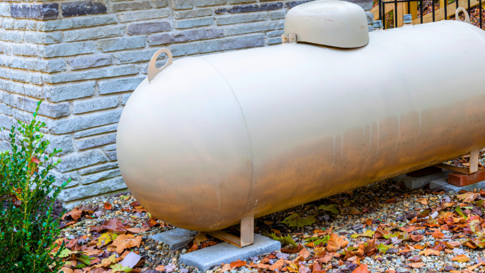 fall propane maintenance tips. a large propane tank outside of a home with fall colored leaves on the ground
